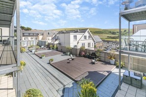 A residential area with a wooden deck, outdoor seating, and a view of houses and hills.