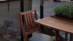 A balcony with a wooden table and chair, overlooking a cityscape with modern buildings during sunset. - Scandinavian Premium Atelier - Spacious Comfort (København)