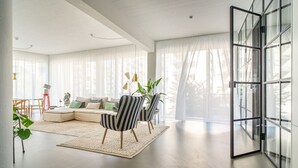 A spacious living room with a large window, a sofa, striped chairs, and a dining area. - Scandinavian Premium Atelier - Spacious Comfort (København)