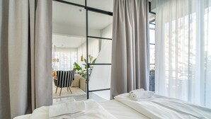 A modern hotel room with a large bed, a view of the city, and a balcony with a chair and plants. - Scandinavian Premium Atelier - Spacious Comfort (København)
