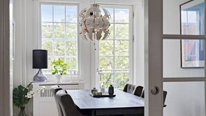 Un comedor con una mesa de madera, sillas, una lámpara colgante, una planta en maceta y un radiador.