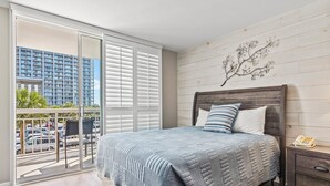 A bedroom with a bed, a nightstand, a decorative wall piece, and a view of a parking area through a sliding door. - Kingston South Hampton 203 - 2 BD Oceanview Condo (North Myrtle Beach)