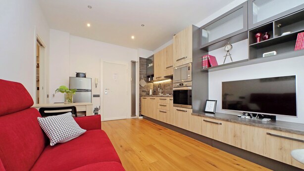 A modern kitchen with wooden cabinets, a large TV, and a red sofa with a patterned pillow. - Modern Apartment in Rome 200 meters from Metro Line A


 (Roma)