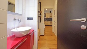 A modern bathroom with a white sink and red cabinets, a hallway leading to a kitchen with wooden cabinets and a refrigerator. - Modern Apartment in Rome 200 meters from Metro Line A


 (Roma)