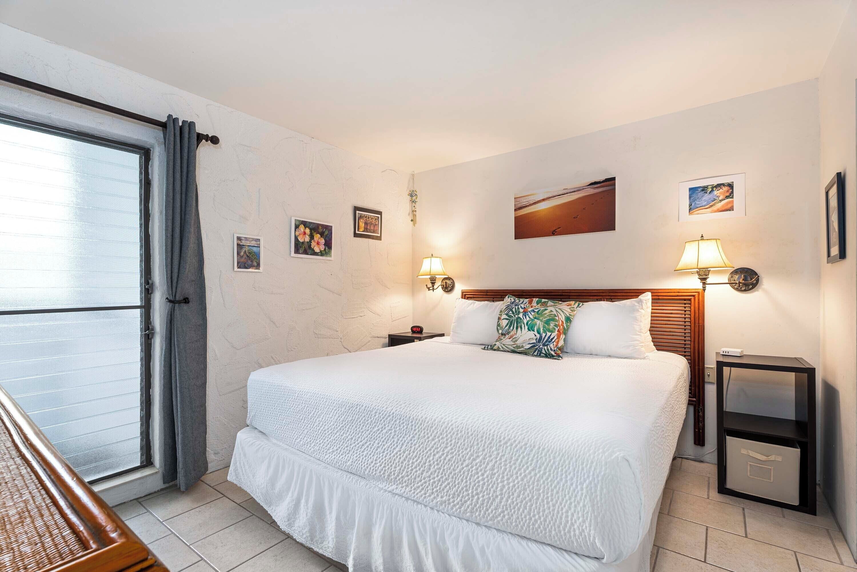 A hotel room with a large bed, two bedside tables with lamps, a small nightstand, a window with curtains, and a view of the outside.
