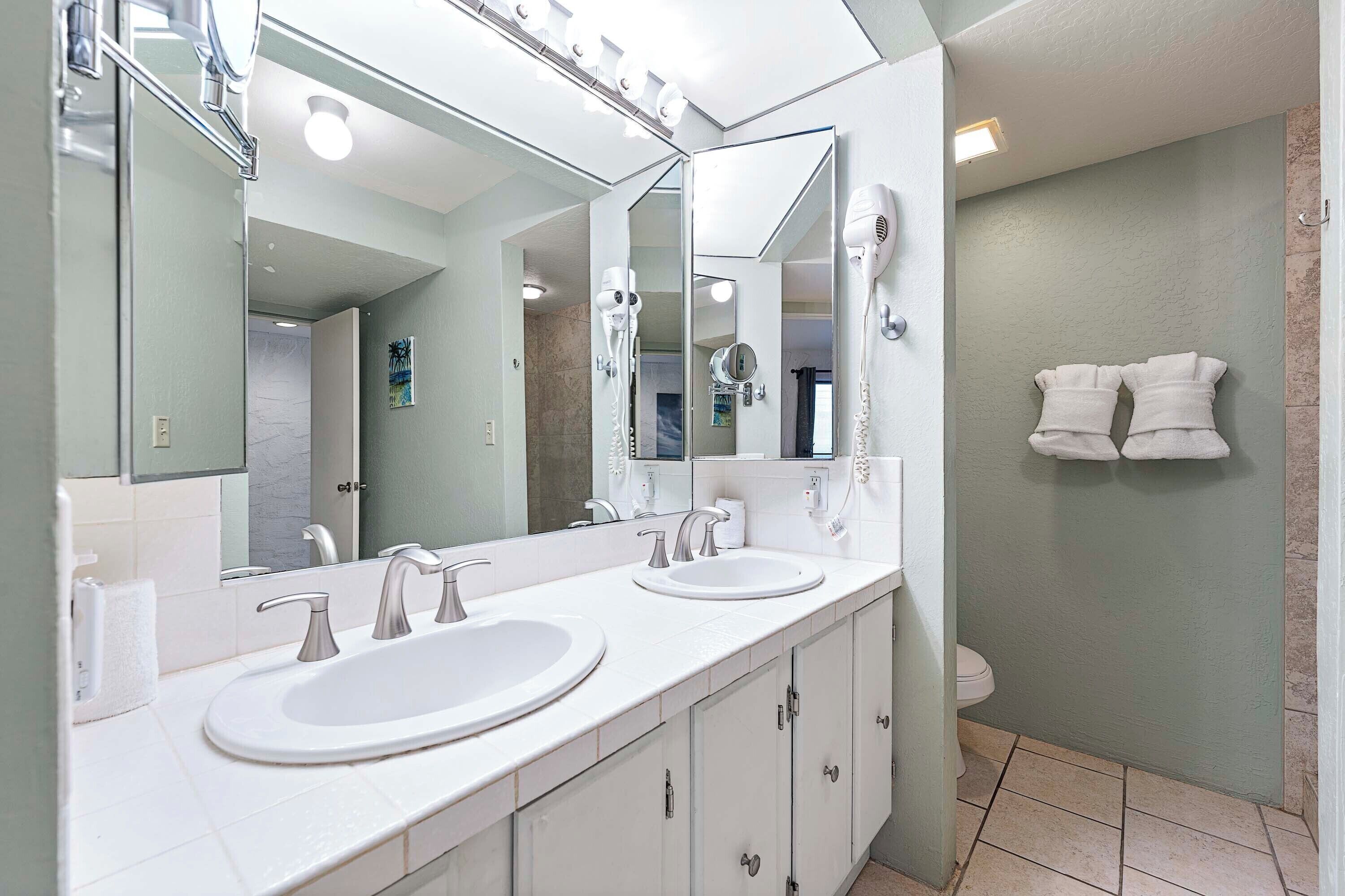 A bathroom with two sinks, a large mirror, and a hairdryer mounted on the wall.