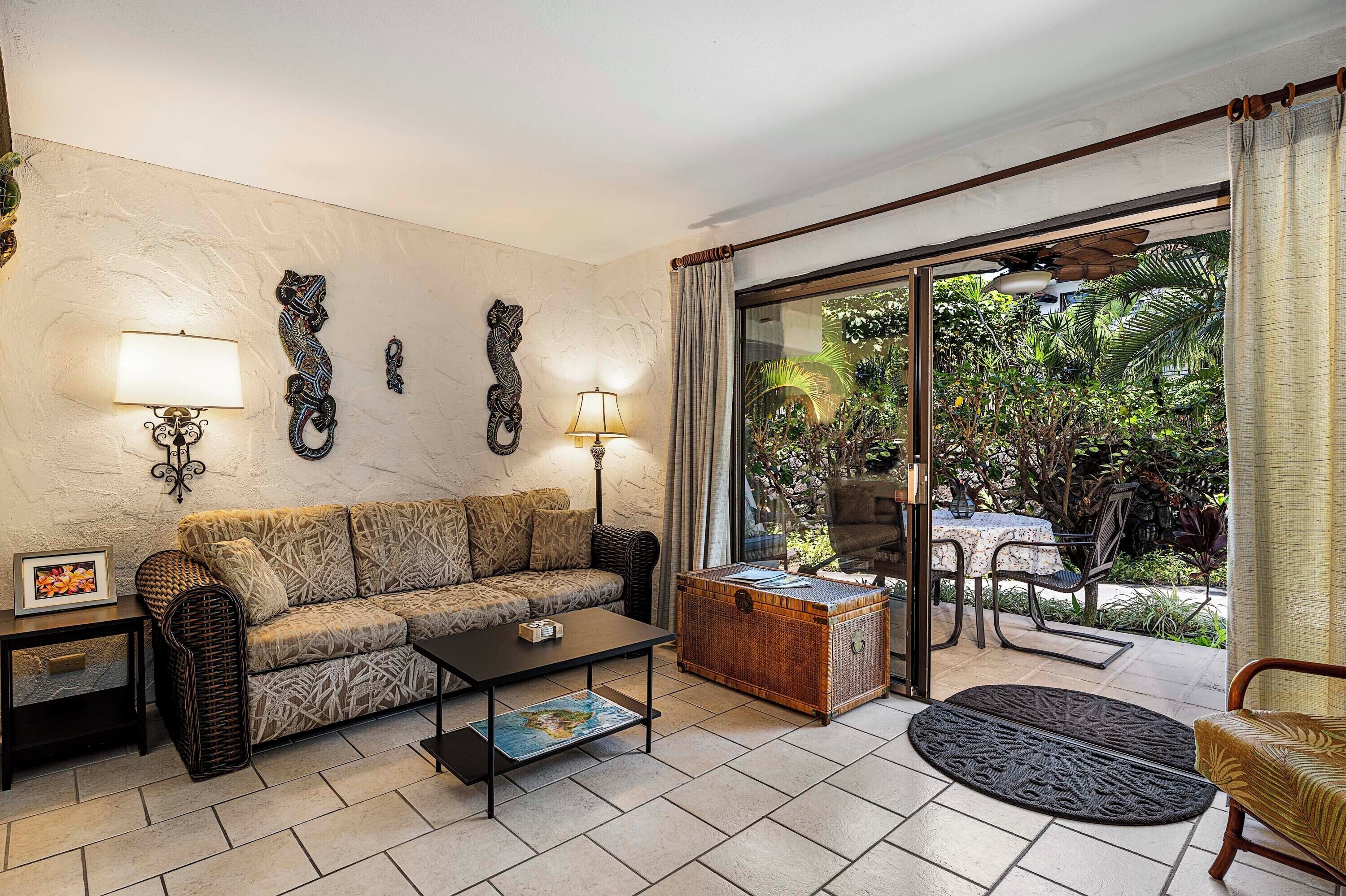 Sala de estar con sofá, mesa de centro y vista a un jardín por una puerta corrediza de vidrio.