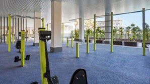 A modern gym with exercise equipment, a blue carpet, and a view of buildings outside. - Holiday Home with Pool by Costarentals - Ref 251 (Las Lagunas de Mijas)