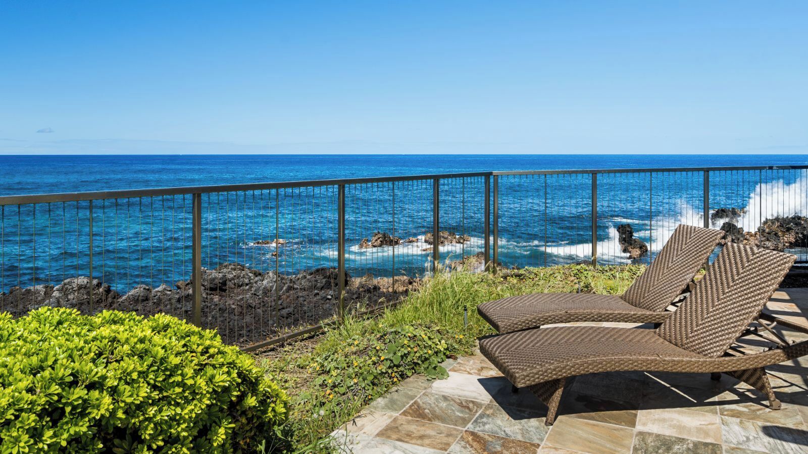 En balkon med to fletloungestole med udsigt over en klippefyldt kystlinje og havet.