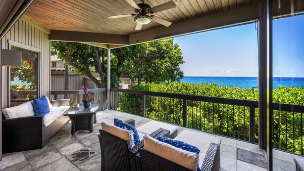 A covered outdoor seating area with wicker furniture and a view of the ocean.