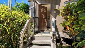 A wooden staircase leading to a door with a glass panel, surrounded by lush greenery.