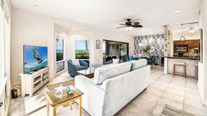 A spacious living room with a large sofa, a television, and a dining area with a kitchen in the background.