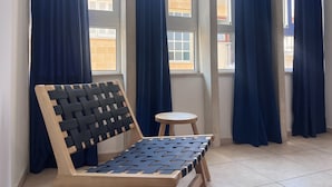 A room with a wooden bench with a black and white woven backrest, a small round table, and large windows with blue curtains. - Phaedrus Living: Hoopoe Residencies 105 (Nicosia)