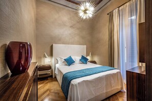A hotel room with a large bed, a nightstand, a vase, a lamp, and a modern chandelier. - YID SMN LUX (Florence)
