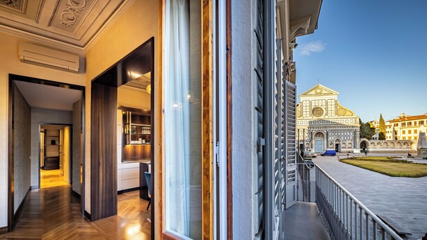 A hotel corridor with wooden flooring, large windows, and a view of a historic building in the background. - YID SMN LUX (Florence)