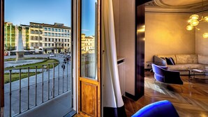 A modern hotel room with a large window overlooking a cityscape, a cozy seating area with a sofa and armchairs, and a stylish pendant light fixture. - YID SMN LUX (Florence)