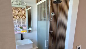 Ein modernes Badezimmer mit einer Glaskabine zur Dusche, einem Waschbecken mit Spiegel und einer hängenden Leuchte.