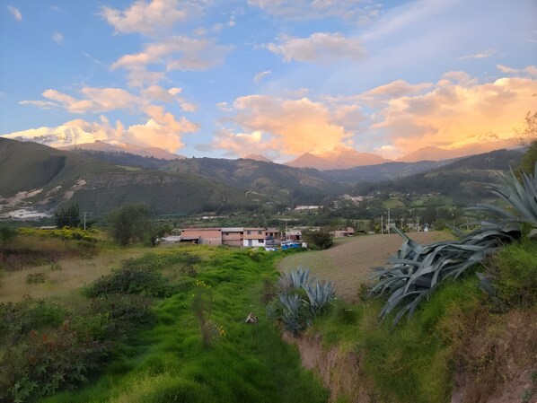 A rural landscape with a small cluster of buildings, a clear sky, and a mountain range in the background.