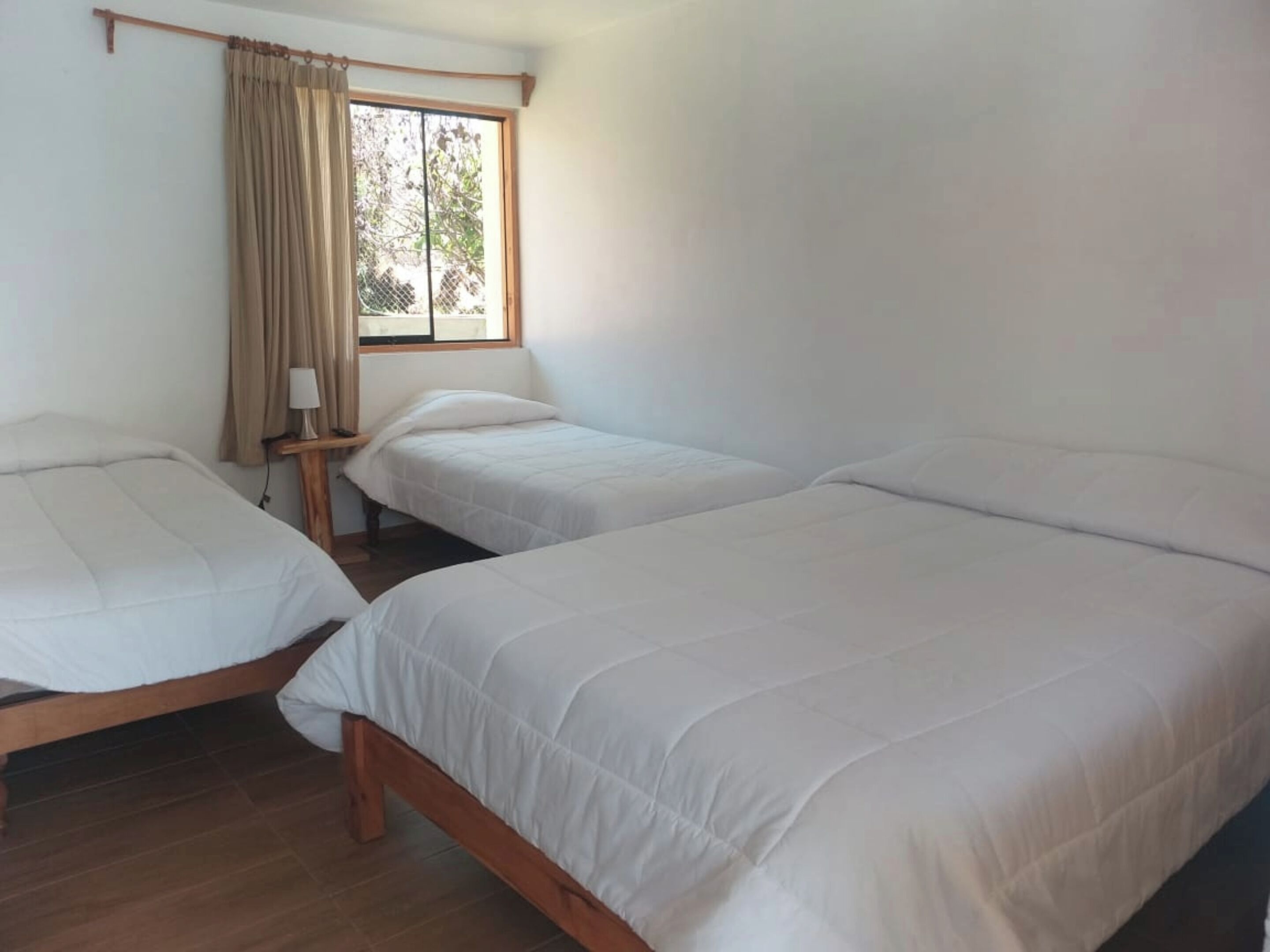 Ein Zimmer mit zwei Einzelbetten, einem fenster mit Vorhängen und einem Nachttisch mit Lampe.