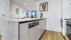A modern kitchen with a marble island, built-in dishwasher, and a large window offering a city view.