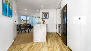 A modern kitchen with white cabinetry, a marble island, and a dining area with a glass partition.