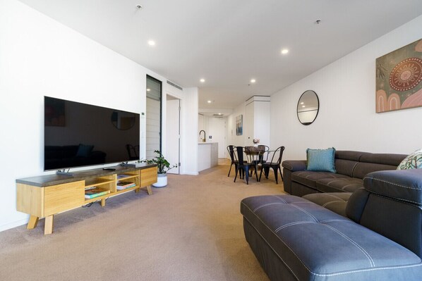 Uma sala de estar moderna com uma TV de tela plana, um móvel para entretenimento de madeira, um sofá de couro preto e um espaço de jantar com mesa e cadeiras.
