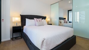 A modern hotel room with a large bed, two bedside tables with lamps, a glass partition wall, and a large mirror.