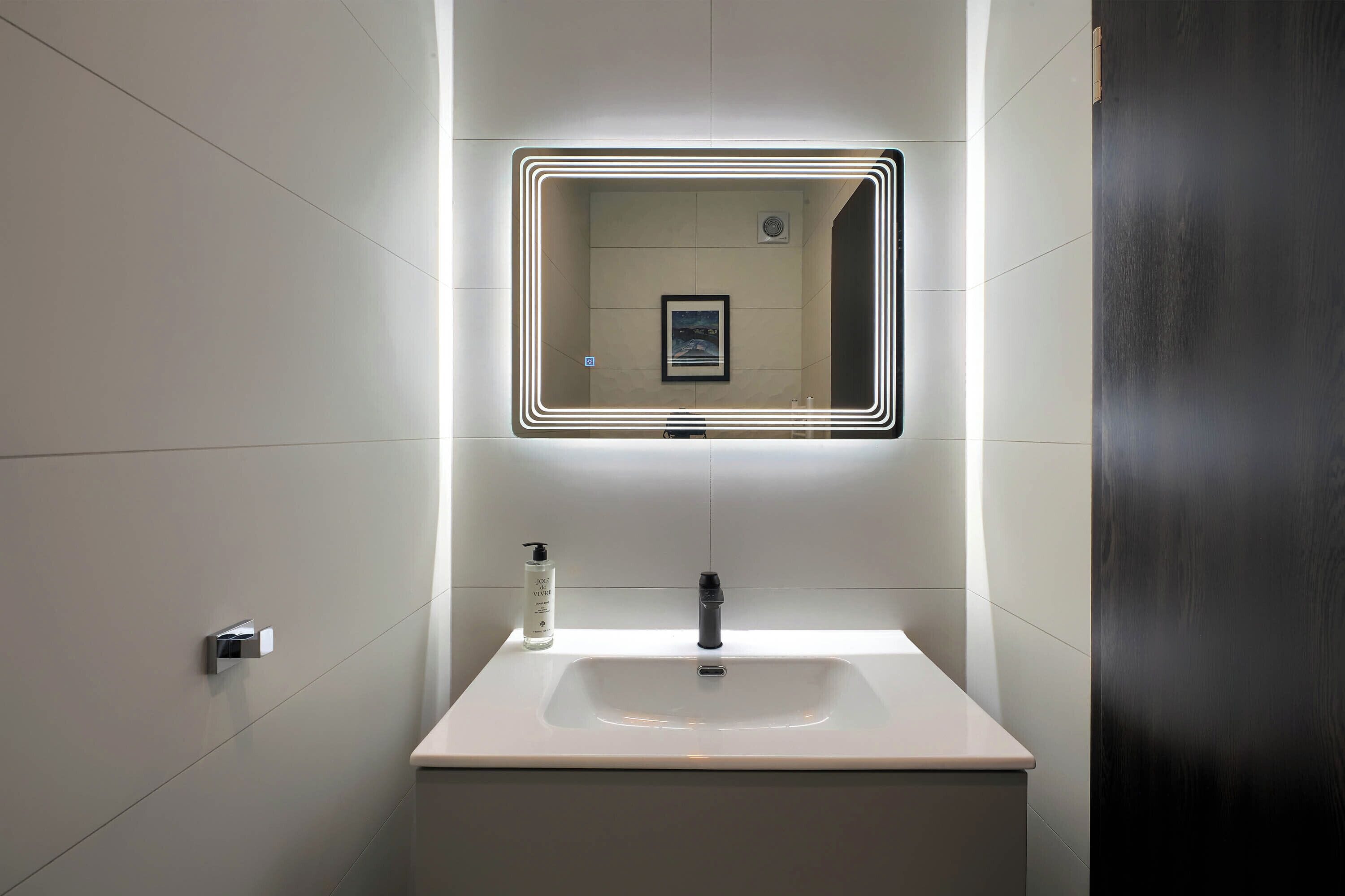 Un baño moderno con un lavamanos blanco, un espejo con marco iluminado y una botella de jabón para manos.