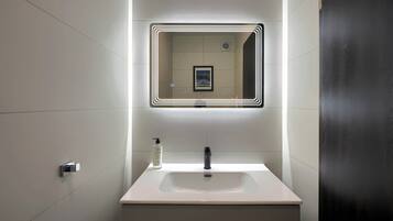 Un baño moderno con un lavamanos blanco, un espejo con marco iluminado y una botella de jabón para manos.