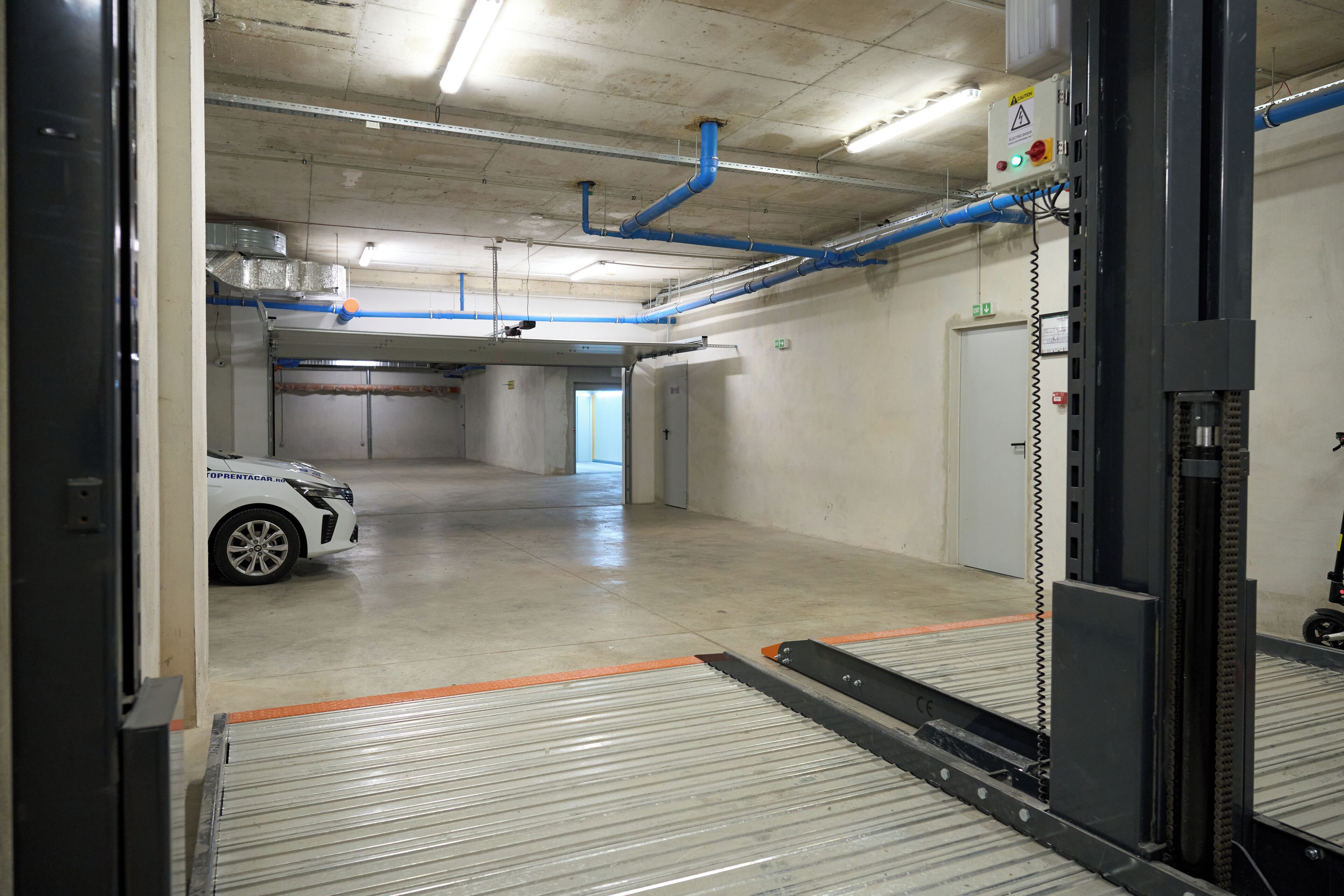 Un garage con un'auto bianca, pavimenti in cemento e tubature blu al soffitto.