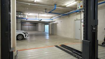 Un garage con un'auto bianca, pavimenti in cemento e tubature blu al soffitto.