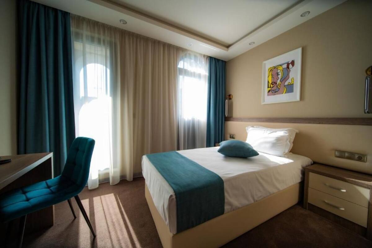 A hotel room with a bed, a desk, a chair, and a painting on the wall.