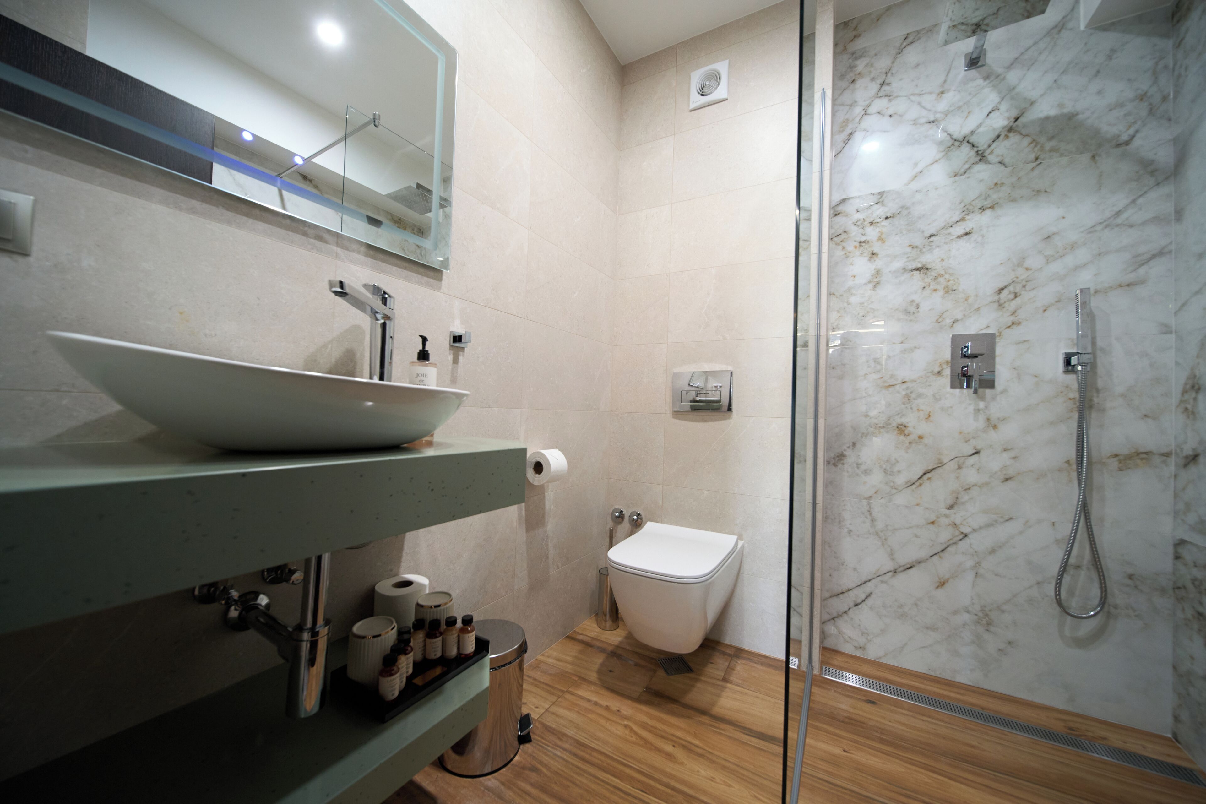 Un baño moderno con ducha envuelta en vidrio, un lavamanos blanco con un lavabo y un inodoro.