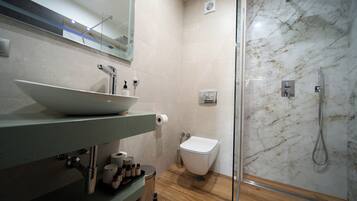 Un baño moderno con ducha envuelta en vidrio, un lavamanos blanco con un lavabo y un inodoro.