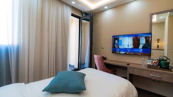 Habitación de hotel con cama, escritorio, televisión y ventana con cortinas.