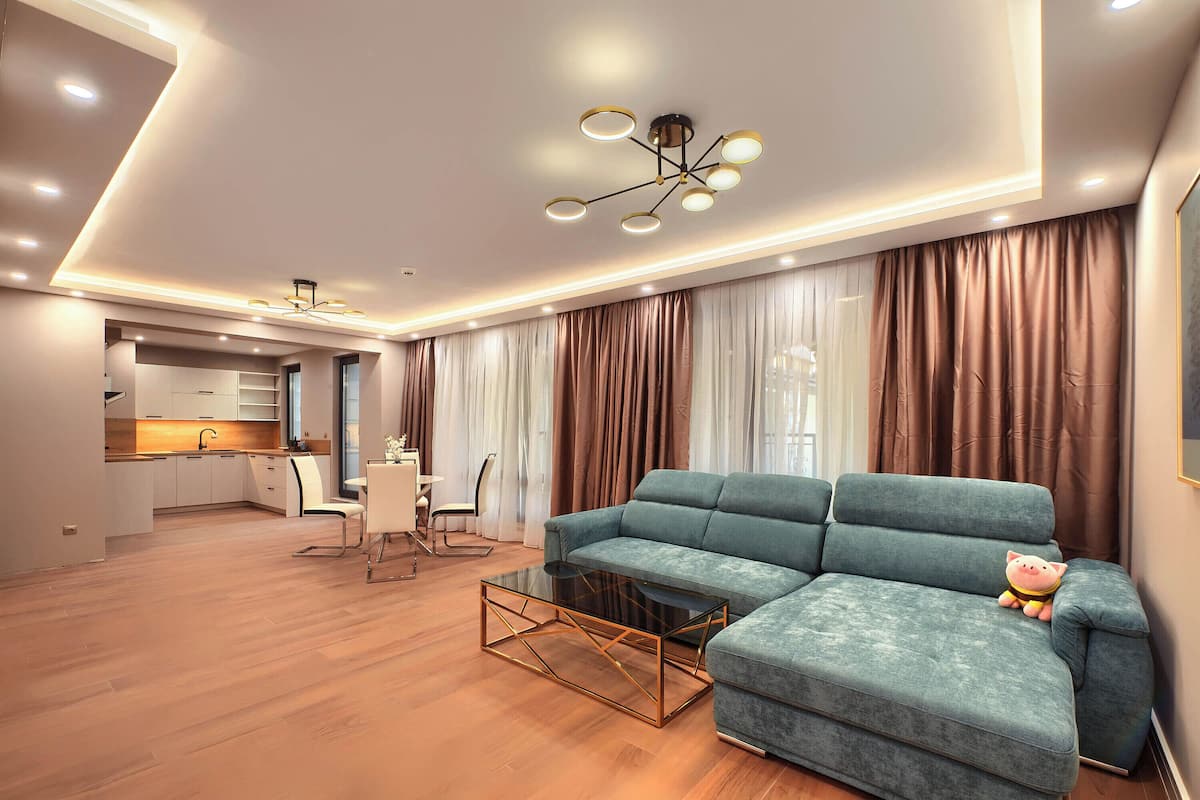 A modern living room with a sectional sofa, a glass coffee table, and a dining area with a white table and chairs.