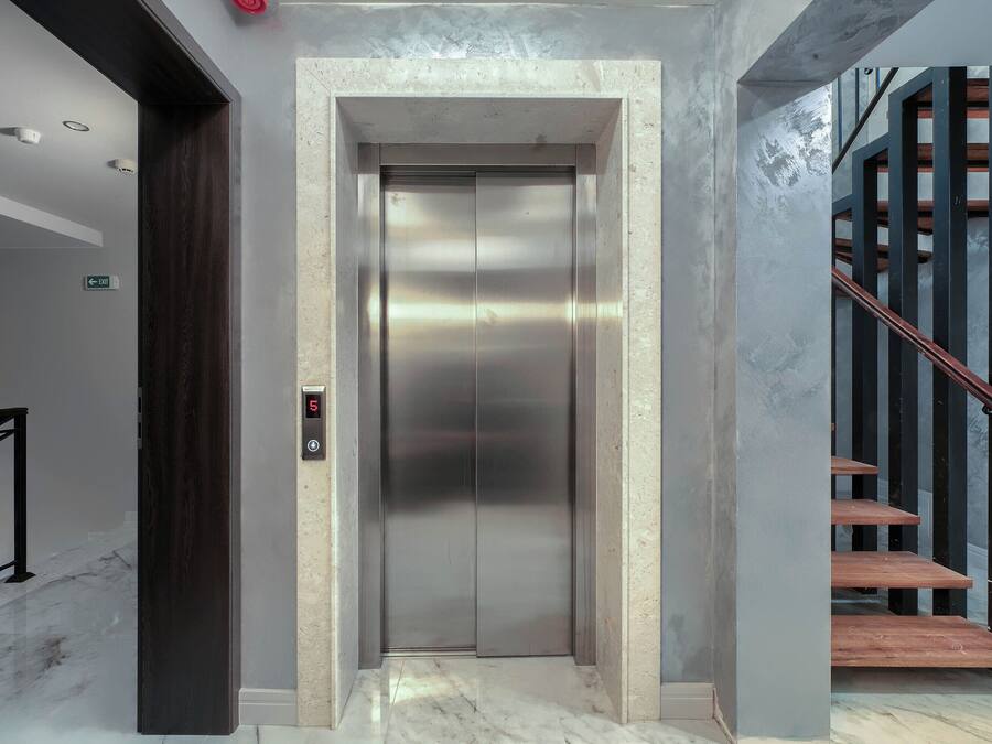 Un ascensor con detalles metálicos, una pantalla digital y piso de mármol.