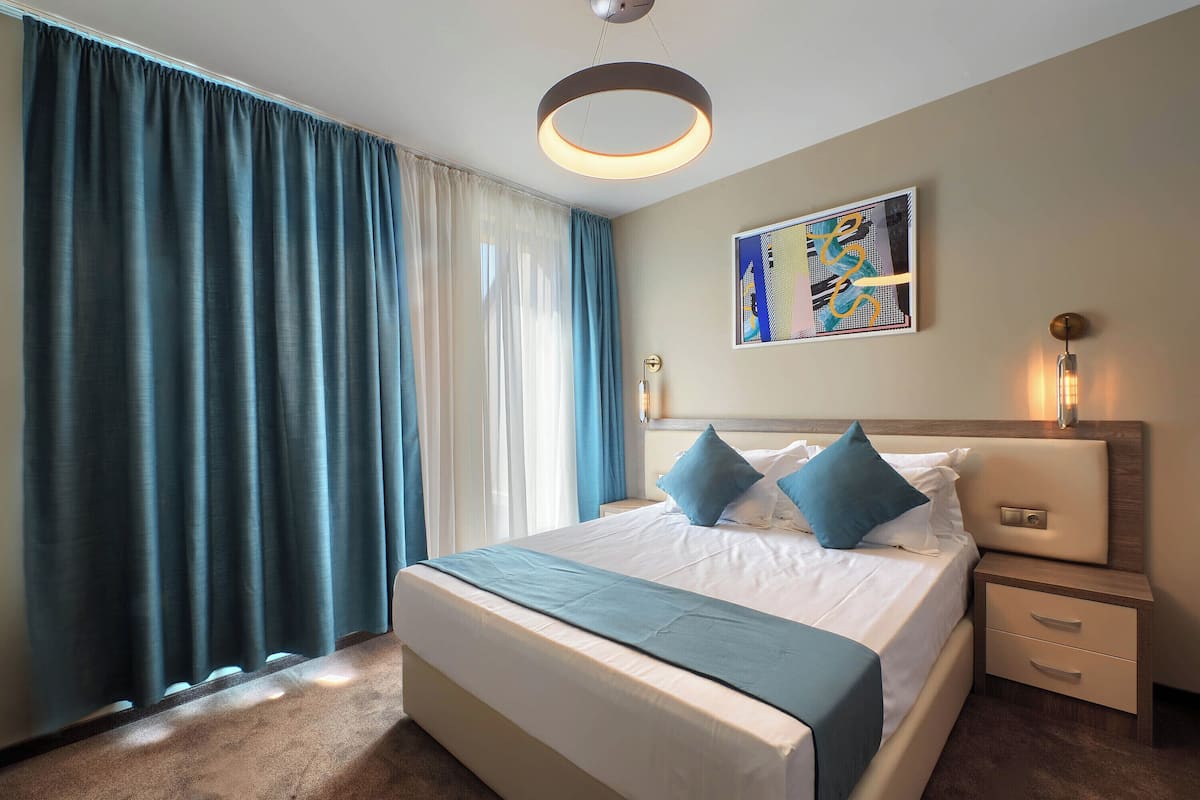 A hotel room with a large bed, a bedside table with a lamp, and a painting on the wall.