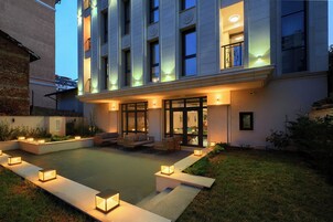 A modern building with a covered outdoor seating area, a pool, and outdoor lighting.