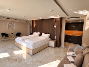 A modern bedroom with a large bed, a small bedside table, a built-in wardrobe, and a seating area with a sofa.