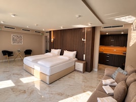A modern bedroom with a large bed, a small bedside table, a built-in wardrobe, and a seating area with a sofa.