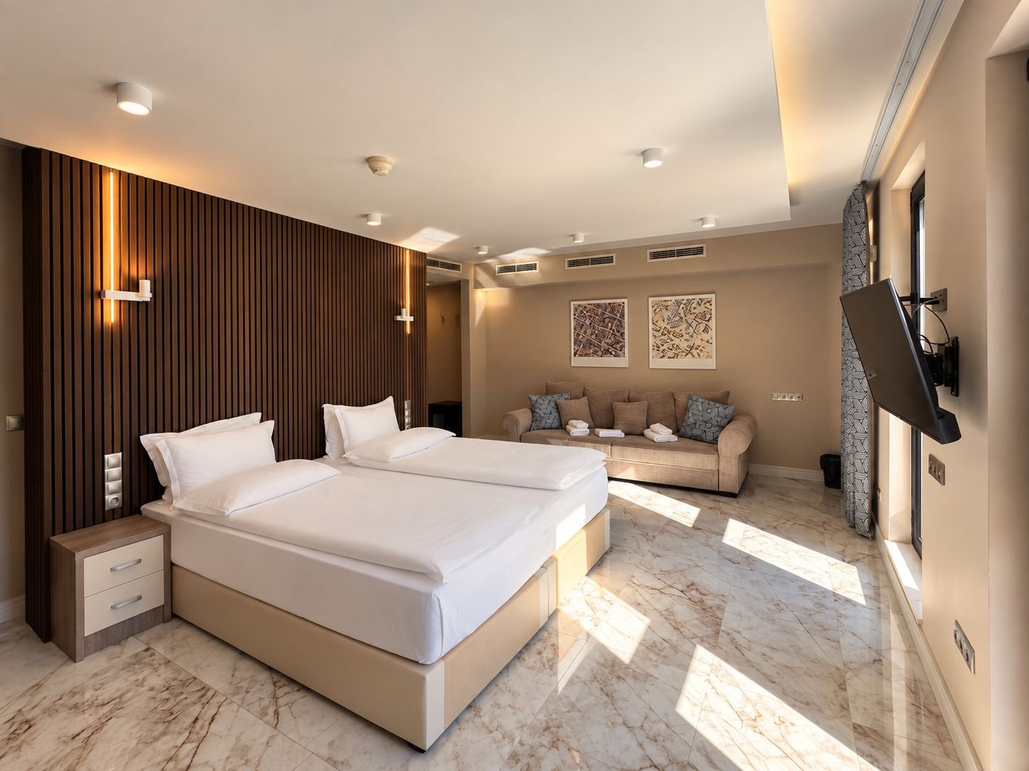 Una habitación de hotel moderna con una cama grande, mesitas de noche, un sofá y un televisor de pantalla plana montado en la pared.