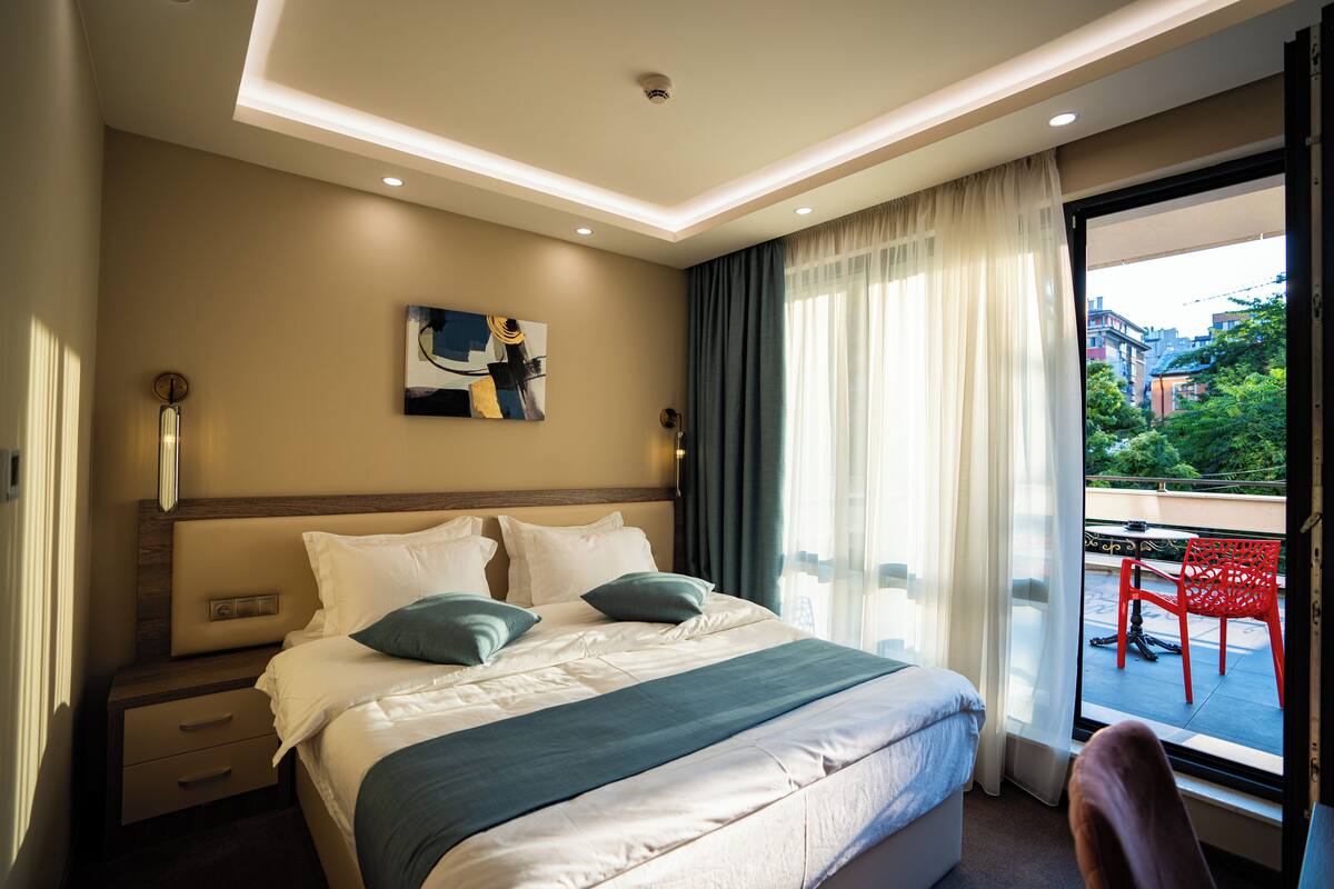 A hotel room with a large bed, a bedside table, a chair, and a view of the outdoors.