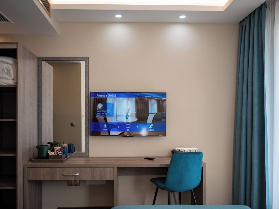 Een hotelkamer met een bed, bureau, stoel, een aan de muur bevestigde televisie en een raam met gordijnen.