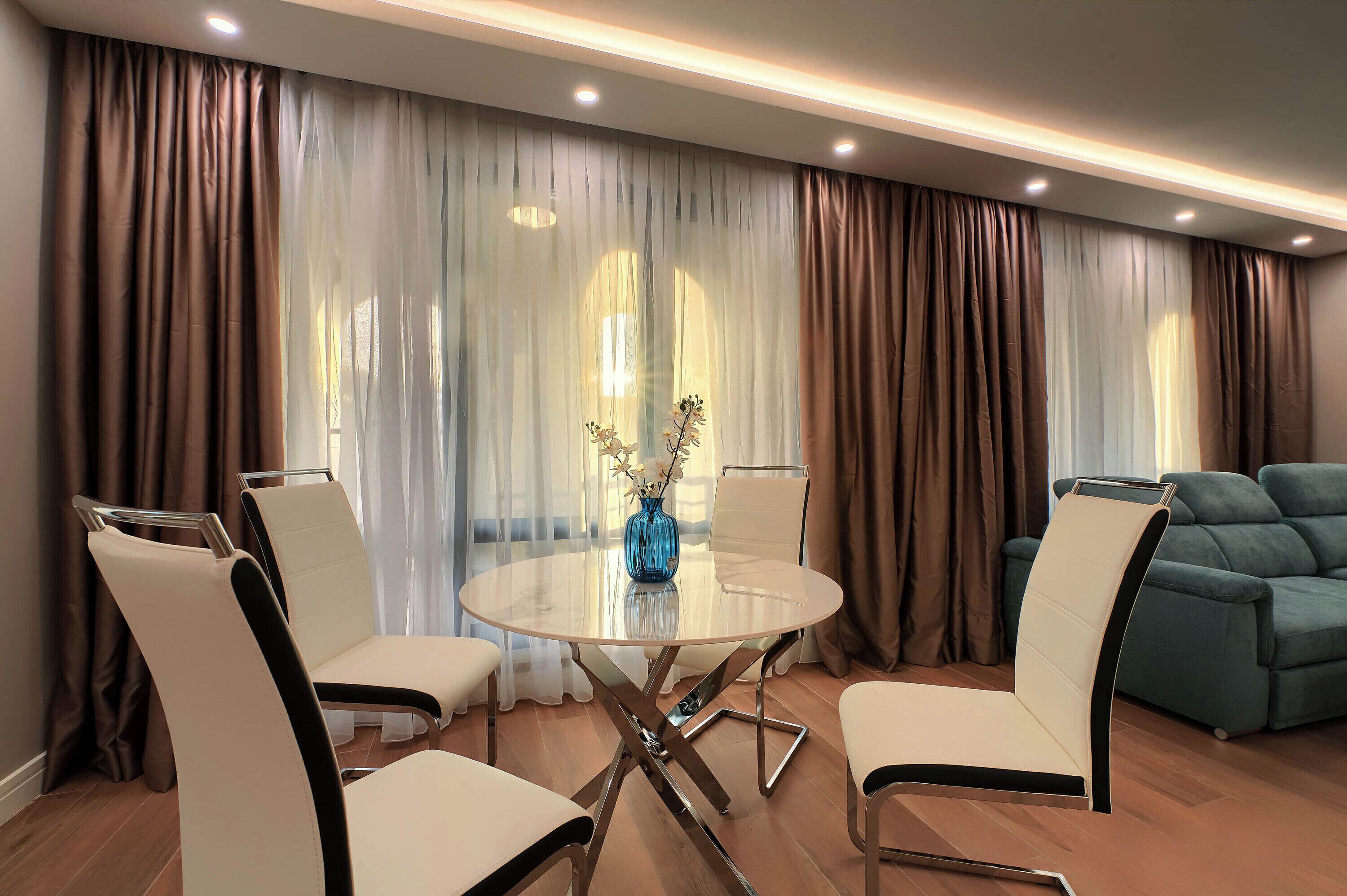 Un salón moderno con una mesa redonda de cristal, sillas blancas y negras, un jarrón azul y un sofá color turquesa.
