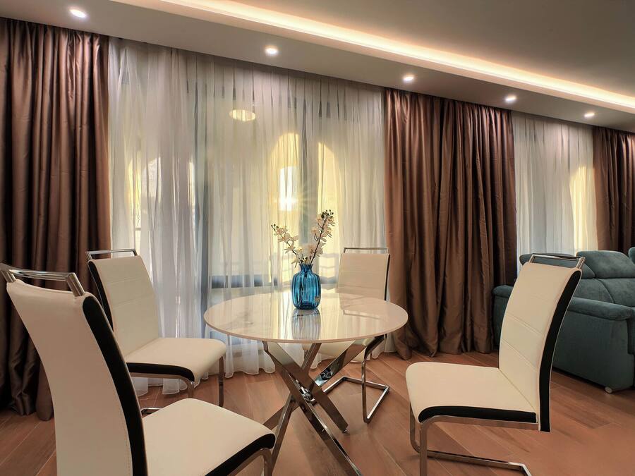 A modern living room with a round glass table, white and black chairs, a blue vase, and a teal sofa.