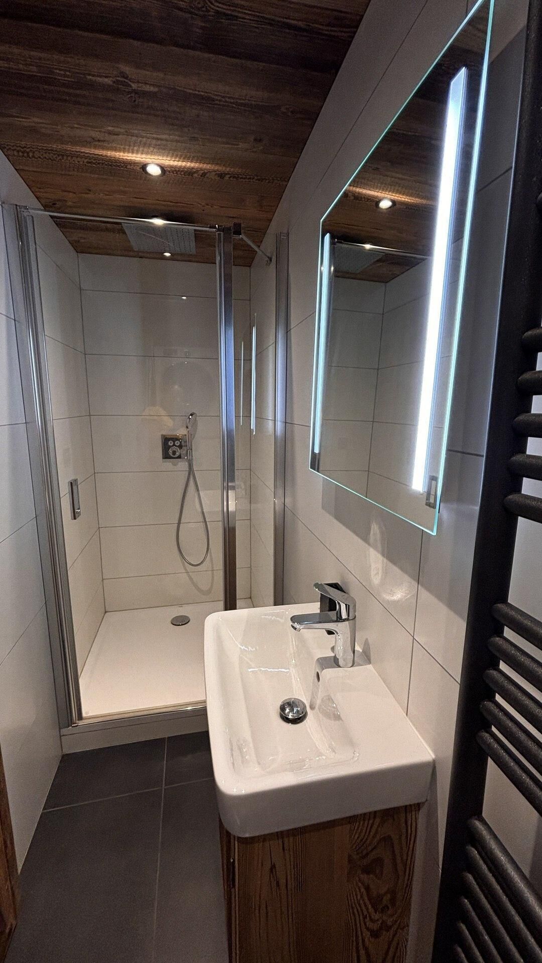 A modern bathroom with a glass shower enclosure, a white sink, and a large mirror with integrated lighting.