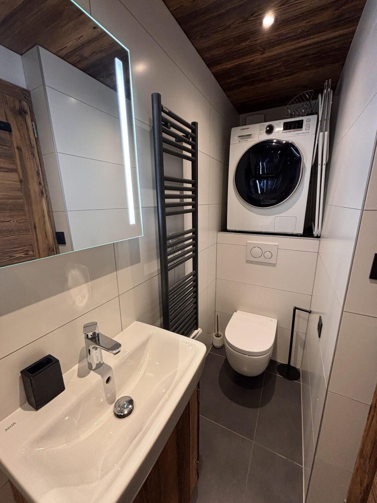 A modern bathroom with a white sink, a toilet, and a built-in washing machine.