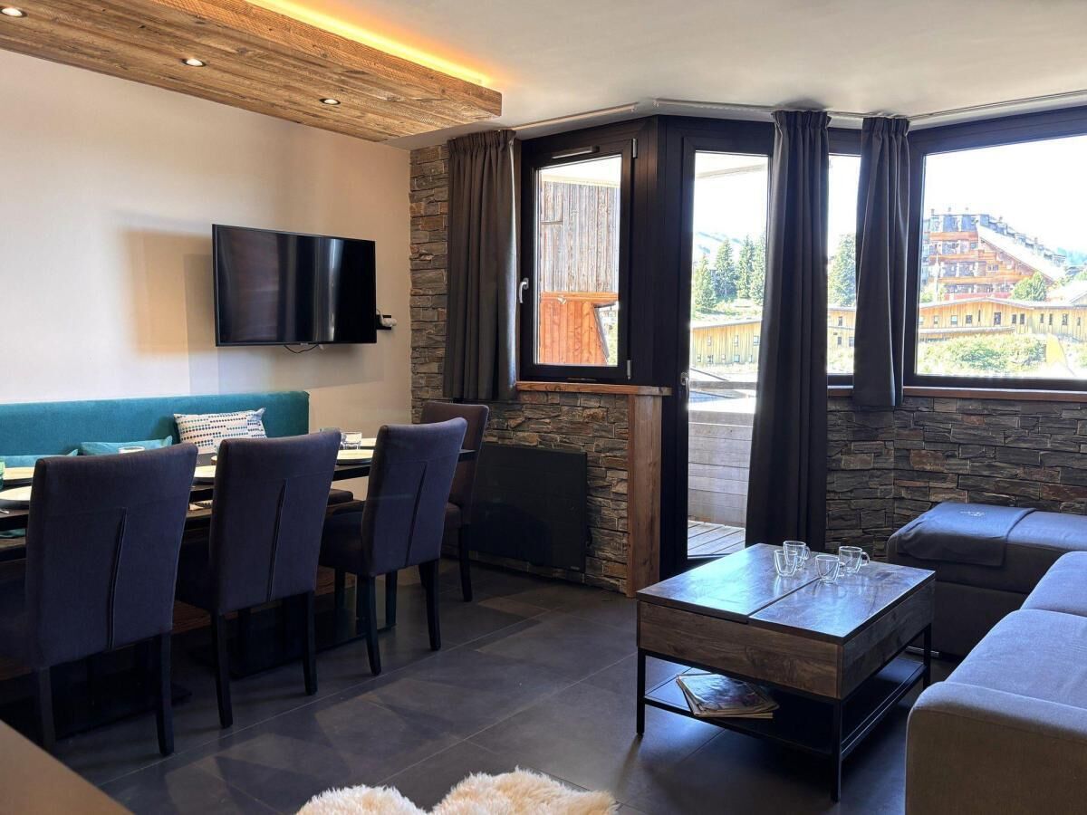 Een moderne woonkamer met een eetgedeelte, een open haard en grote ramen met uitzicht op een gebouw en bomen.