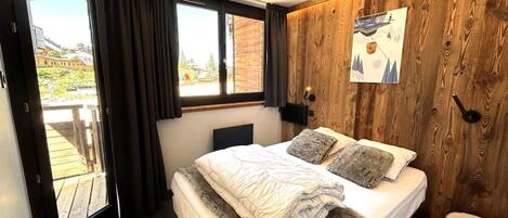 A bedroom with a bed, a window, a wooden wall, and a view of the outside.